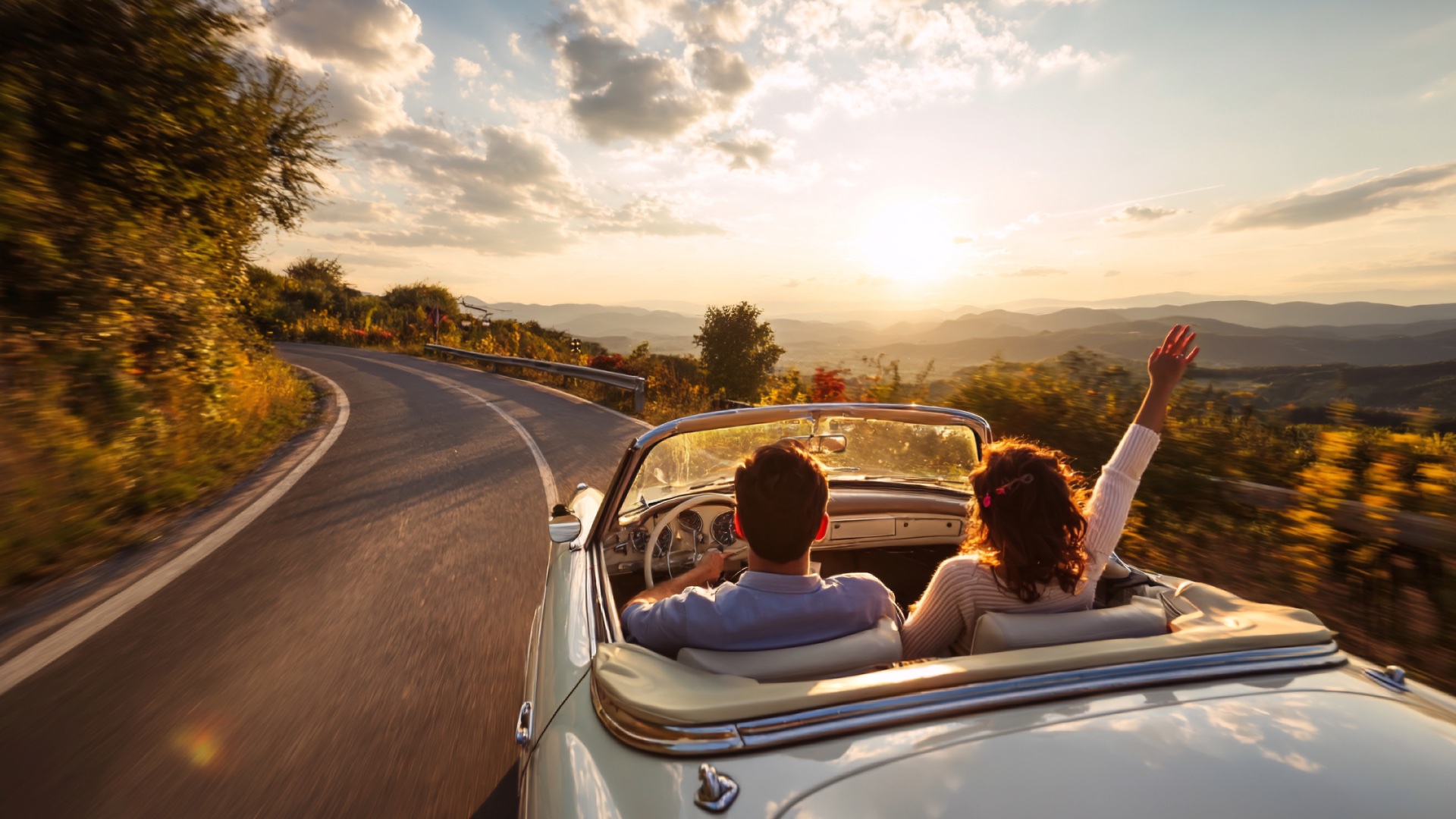 Classic convertible driving along a mountain road at sunset